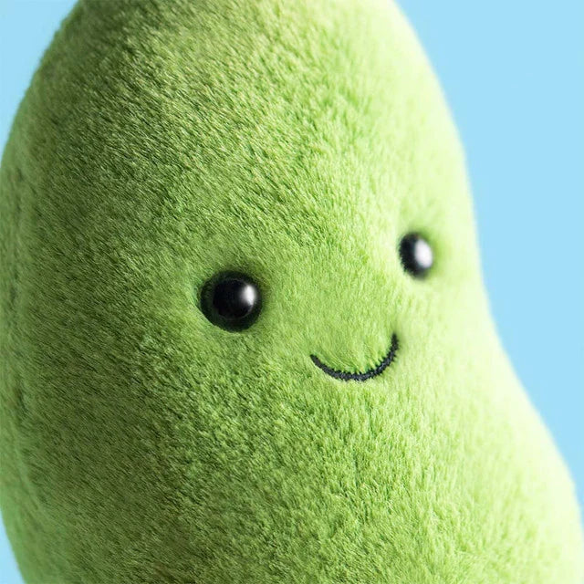 Plush green toy resembling a bean with a smiling face against a blue background