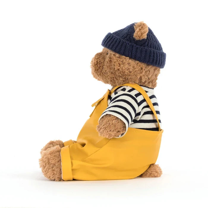 Teddy bear wearing a yellow raincoat, striped shirt, and navy hat on a white background