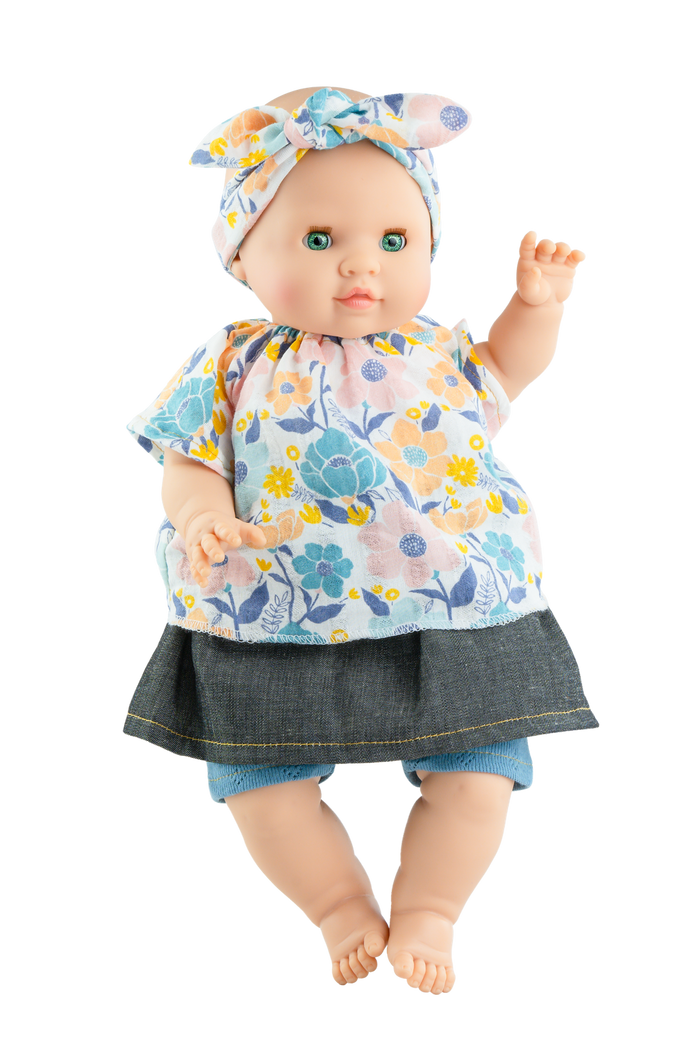 A soft body doll with a vinyl head and limbs, dressed in a floral skirt and a patterned top, with a bow on the head.