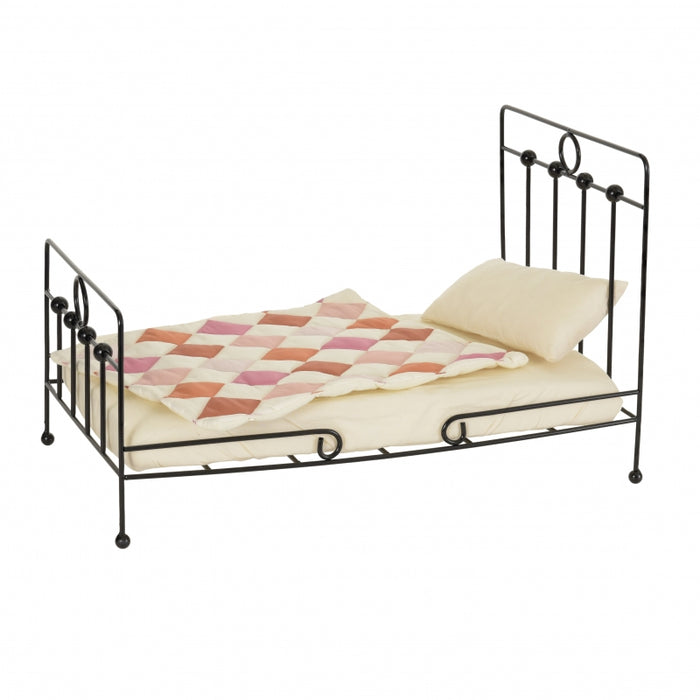 A traditional-style iron doll bed with patchwork quilt, pillow, and mattress.