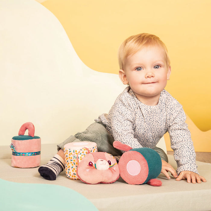 Baby playing with colorful soft toys against a yellow background