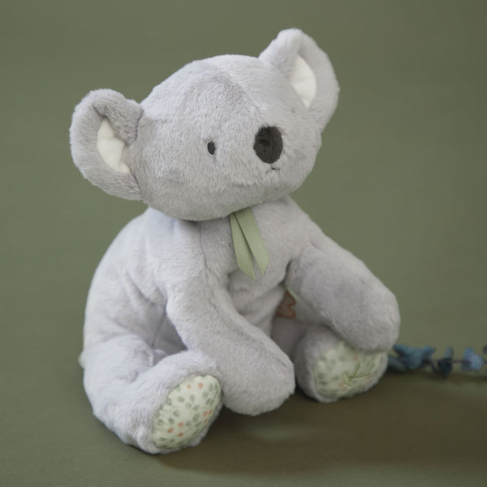 Grey koala soft toy with green neck bow sitting on a sage green bakground