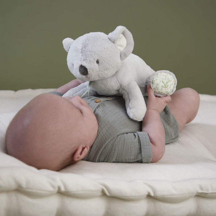 Baby lying on a white mattress cuddling a grey koala soft toy