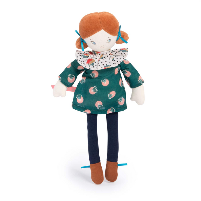 A plush doll with orange hair tied with blue bows, wearing a green dress with a pink and white pattern, a white ruffled collar with black polka dots, dark navy pants, and brown shoes, photographed on a white background.