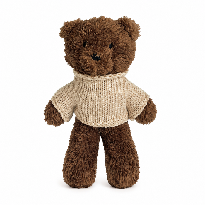Brown teddy bear wearing an oat colour knitted sweater, standing against a white background.