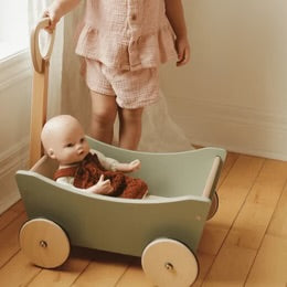 Child with a toy stroller containing a doll on a wooden floor.
