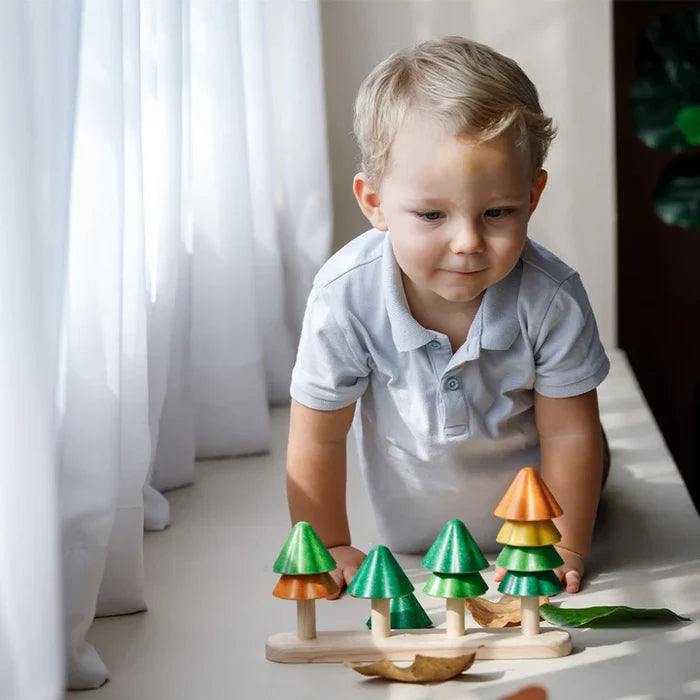 Child playing with a set of colorful wooden trees indoors.