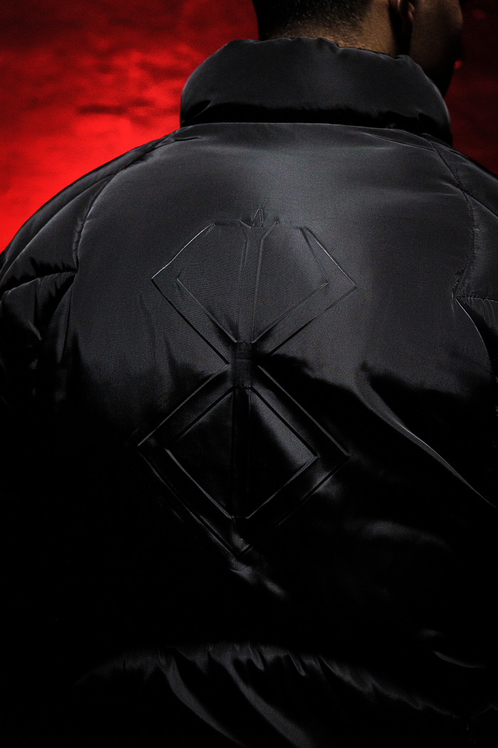 Black Tormented puffer jacket with a geometric pattern on the back against a red background